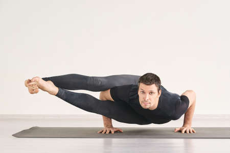 Strong man stand at Astavakrasana. Fitness yoga exercise. Pilates asana. Male gymnast home class....