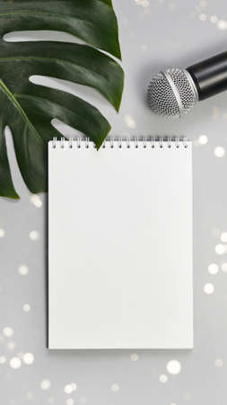 Podcast concept. White notebook with blank sheet. Black microphone and green monstera leaf. Audiobook and podcasting. Audio technology. Home school teaching. Vertical with copyspaceの写真素材