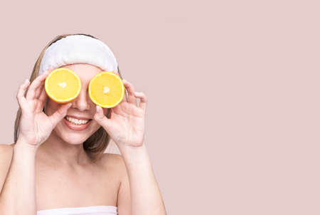 Girl hold orange slice. Citrus fruit hidding face. antioxidant home care routine. Facial energy product. Laughing portrait. Modern nature cosmetic. Ecology beautyの写真素材