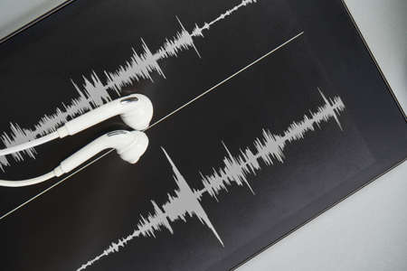 Podcast record. earbuds and sound track at tablet. Grey monochrome. Audiobook and podcasting. Audio technology. Home school teaching. Edit episodeの写真素材