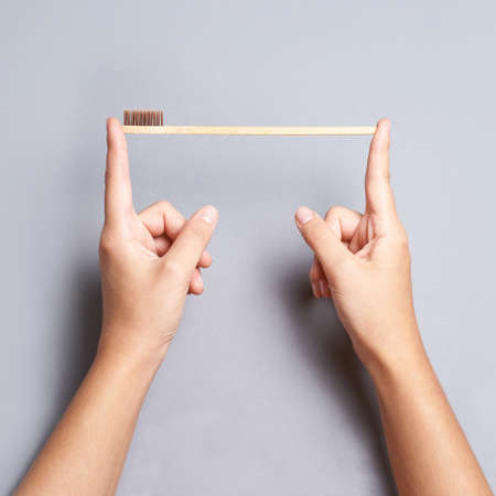 Hands hold one bamboo eco tooth brush. brown color. Dental care. Morning oral routine. Grey background. Copy space. Washing prevention hygiene. Squareの写真素材