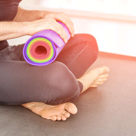 Person holding yoga mat at knee. Sport equipment concept. Pilates teacher with rolled color workout equipment. Man fitness health mockup. Copyspace bannerの写真素材