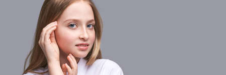Beauty girl portrait. Young woman. Hand near nead. Face massage concept. White shirt. Cosmetology facelift laser. Medical rejuvenation scrub. Skin care hygiene. Grey background. Horizontal bannerの写真素材