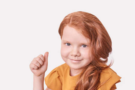 Red hair little girl. Thumb up gesture. Approve hand symbol. Female face. Looking at camera....