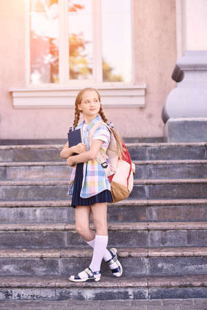 Young schoolgirl with backpack. Lifestyle going to classroom. Outdoor autumn park. Children learn smart. Street student. Happy preschool kid. Back to school. Near buildingの写真素材