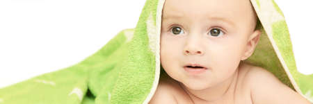 Cute little baby. Under bath towel. Happy kid portrait. White background. Lying at home bed. Infant playing. Beautiful bear. New human. Face skin care. Good emotion. Horizontal banner. Copyspaceの写真素材