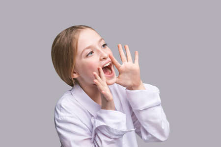 Girl shout. Little lady scream about sale. Looking side. Pretty kid with hands near head. Child portrait. Modern loud. Positive emotion. Sound on. Yelling face. Rumor conceptの写真素材
