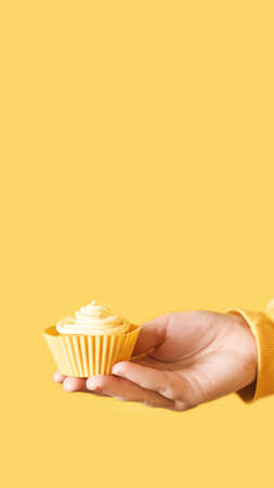 Yellow monochrome bakery. Sustainable cupcake cup. Hold in hand. Gold maffin cream. Trendy colourful desert. Bright birthday gift. Vertical banner for story. Copyspaceの写真素材