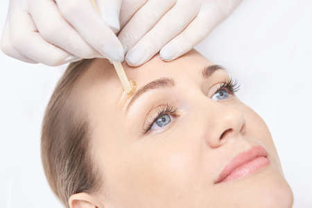 Hot hair removal depilation. Female skin routine. Sugar bodycare. Wax Eyebrow correction. Professional cosmetologist help girl. Sugaring bodycare cosmetics.の写真素材