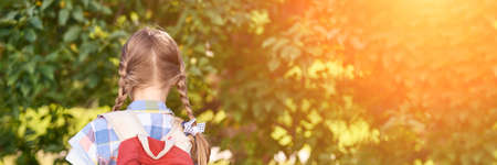 American portrait of schoolgirl. Preschool kid. Little happy girl outdoors. Pretty female person. Adorable candid children. Summer park. Back view with backpackの写真素材