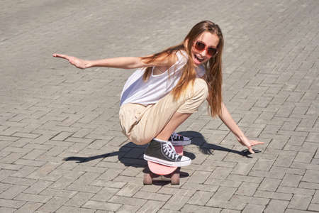 Young woman show skateboard deck. Pink color. Sun shade. High quality photo. Skatepark equipment....