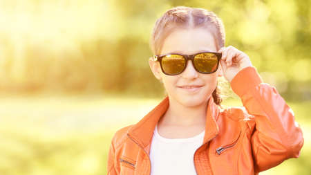 Little girl with sun eyeglasses. Bright dress. High quality photo. Smiling female person. Orange and green color. Child like smart businesswoman. Cute happy kid. Positive emotionの写真素材
