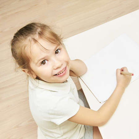 Kid education. Top view at school girl. Clever student writing homework. Mockup with copyspace. Smiling little woman. Kindergarten female portrait. Look in camera. Write or draw at blank notebook.の写真素材
