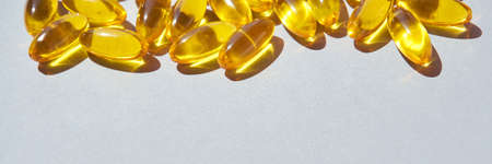 Omega3 gel capsule. Sun shadow. Yellow vitamin. Health eating. Dietology drug. Fish oil supplement. Nurtitional concept. Golden color softgel collagen. Grey background. Medicine immunity cosmeticsの写真素材