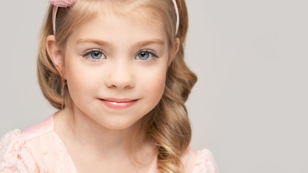 Little pretty girl portrait. Studio shot. Cute kid face. High quality photo. Smiling children. Blond hair. Caucasian female people. Beauty head. Grey background. American healthy person. Pink dressの写真素材