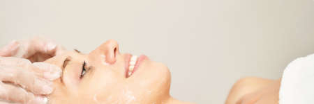 Face massage at spa salon. Doctor hands. Pretty female patient. Beauty treatment. Healthy skin procedure. Young woman head. Light background. Scrub rejuvenation. Facial dermatology mask. Detox therapyの写真素材