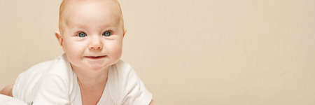 Cute small boy lying at bed. Childhood concept. Light background. Smiling child. Happy emotion. Copyspace. Stay home. Mockup. Horizontal banner. White clothesの写真素材