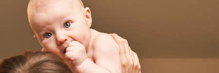 Cute small boy at mother hands. Childhood concept. Serious child. Calm emotion. Copyspace. Stay home. Blue eyes. Horizontal banner. Family careの写真素材