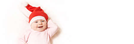 Cute small boy lying at bed. Childhood christmas concept. Light background. Smiling child. Xmas red hat. Copyspace. Stay home. Mockup. Horizontal banner. Pink female clothesの写真素材