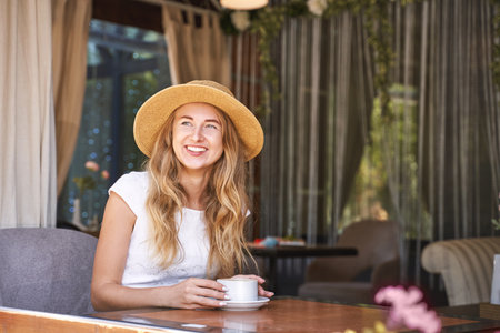 Young woman drinking coffee at street cafe. Staycation tourist. Female person in summer hat. Positive emotion. Smiling people. Dreaming about vacationの写真素材