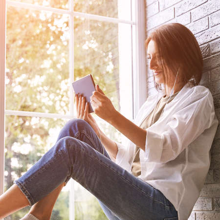 Young woman sitting at windowsill. Working on tablet. Online study concept. Safety lockdown distance...