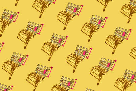Many same shop trolley on yellow bright background. Modern mall concept. Top view repeat layout. Market cart trend wallpaper. Flatlay. Supermarket empty accessoryの写真素材