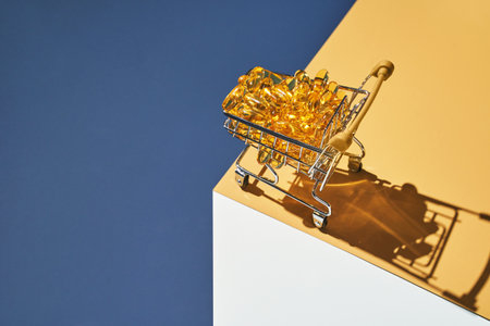 Omega3 gel capsules at shop cart. Sun shadow. Yellow vitamin. Health eating. Dietology drug. Fish oil supplement. Nutritional concept. Golden color softgel collagen. Blue background. Medicine immunityの写真素材