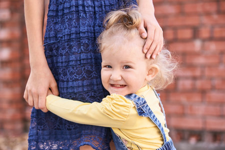 Little girl hug sister leg. Female child portrait. Happy people. Model posing outdoors. Curly hairの写真素材