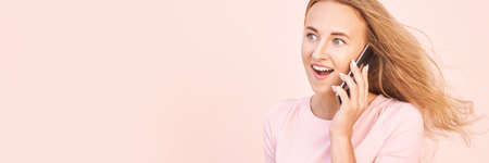 Pretty young woman talking by phone. Happy female person outdoors. Summer business portrait. Lady calling friends or boyfriend. Blonde long hair. Cute adult student at townの写真素材