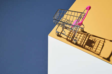 Shop trolley on yellow and blue bright background. Modern mall concept. Isometric trendy layout. Market cart trend wallpaper. Supermarket empty accessoryの写真素材