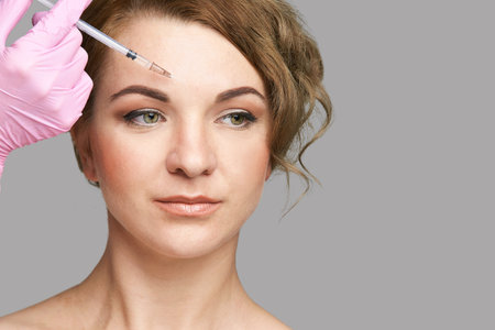 Face needle injection. Young woman cosmetology procedure. Doctor hand in glove holds. Female patientの写真素材