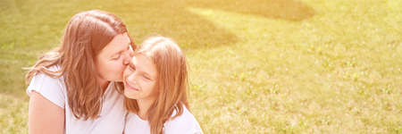 Mother kiss teenage daughter. Outdoor family portrait. Two person together. Happy positive feelings. Casual tshirt. Motherhood lifestyle. Parent relationship.の写真素材