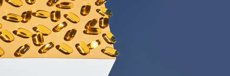 Omega3 gel capsule. Sun shadow. Yellow vitamin. Health eating. Dietology drug. Fish oil supplement. Nutritional concept. Golden softgel collagen. Blue background. Medicine immunity cosmetics. Cubeの写真素材