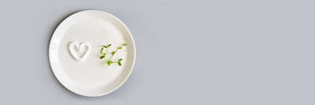Heart shape cream. Beauty lotion. Mayonnaise smear on white plate. Top view with copyspace. White product smear. Valentine concept. Horizontal banner. Green peas. Grey backgroundの写真素材