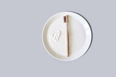 Ecology toothbrush on grey background. Brush on plate. Breakfast concept. Sustainable mouth product. Zero waste lifestyle. Organic accessory. Dental health at home. Biodegradable recycle. Toothpasteの写真素材