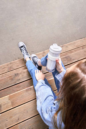 Pretty girl drink beverage outdoors. Buy takeaway coffee in own cup. Caucasian real people. Single female person. Alone. Ecology concept. Positive attractive human. Jeans dress. Sustainable lifestyleの写真素材