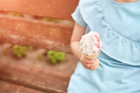 Pretty fun kid eating ice cream at park. Vacation concept. Staycation lifestyle. Family holiday. Summer unhealthy snack. Milk baby food. Waffle cone shape at children hand. Female personの写真素材
