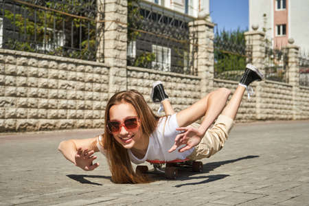 Girl lying on skateboard. Town landscape. Black sneakers. New normal travel. Eco trip. Local city traveller. Staycation lifestyle. Extreme skate riding. Road to school. Funny emotionの写真素材