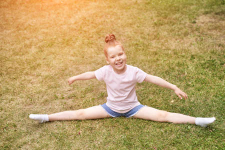 Pretty face. Red hair. Cute school child doing yoga exercise. Active vacation. Small people in leg-split. Happy children concept. Lifestyle action. Watching sport lessonの写真素材