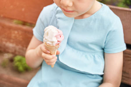 Pretty fun kid eating ice cream at park. Vacation concept. Staycation lifestyle. Family holiday. Summer unhealthy snack. Milk baby food. Waffle cone shape at children hand. Female personの写真素材