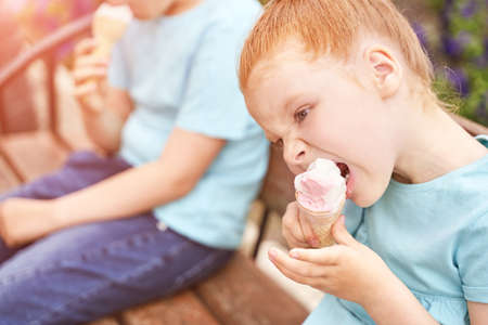 Pretty fun kid eating ice cream at park. Vacation concept. Staycation lifestyle. Family holiday. Summer unhealthy snack. Milk baby food. Waffle cone at children hand. Female person. Sister and brotherの写真素材