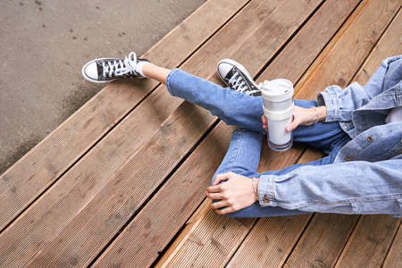 Pretty girl drink beverage outdoors. Buy takeaway coffee in own cup. Caucasian real people. Single female person. Alone. Ecology concept. Positive attractive human. Jeans dress. Sustainable lifestyleの写真素材