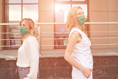 Not touch people in mask portrait. New normal. Corona virus safety. Two women stand at town. Friends. Playground background. Outdoors. Health careの写真素材
