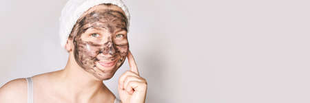 Young woman applying black face mask. Charcoal facial product. Acne and pimple removing. Mud coal...