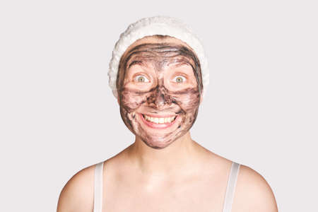 Young woman applying black face mask. Wow emotion. Charcoal facial product. Acne and pimple removing. Mud coal therapy. Fresh dermatology scrub. Copyspace. Cosmetology wellness procedureの写真素材