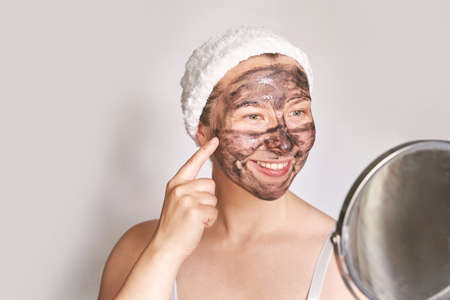 Young woman applying black face mask. Charcoal facial product. Acne and pimple removing. Mud coal therapy. Fresh dermatology scrub. Copyspace. Place for ads text. Cosmetology wellness procedureの写真素材