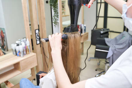 Repair long hair procedure. Haircut at salon. Woman hairstyle. Master hand with brush and fan. Adult female person. Closeup view. Studio equipment. Lady preparation. Blonde dry. Copyspaceの写真素材
