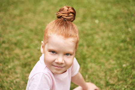 Little girl outdoor portrait. Red hair. Happy baby face. Female person at backyard. American smart schoolgirl. Positive child expression. Smile kid face. Summer timeの写真素材
