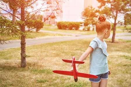 Little girl with airplane toy. Adventure fly concept. Stay home game. Family garden activity. Red hair female portrait. polystyrene childhood pilot. Summer time. Park outdoor aviationの写真素材