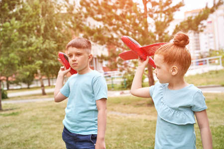 Little girl and boy with airplane toys. Adventure fly concept. Stay home game. Family garden activity. Red hair female portrait. polystyrene childhood pilot. Summer time. Park outdoor aviation. Siblingsの写真素材